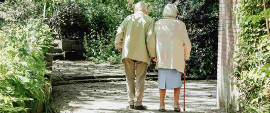 Elderly couple of man and woman with a cane walking in a trail at a park