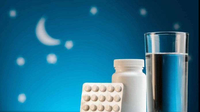 A packet of white pills, a bottle, and a glass of water on a night background with stars.