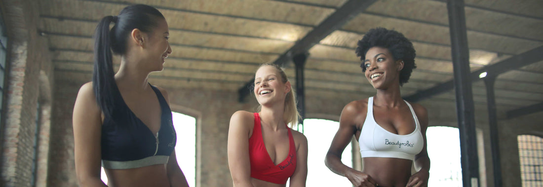 Three women sitting in a gym working out and chatting.