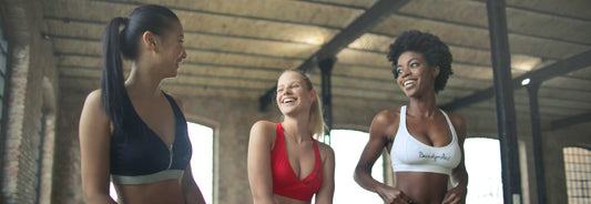 Three women sitting in a gym working out and chatting.