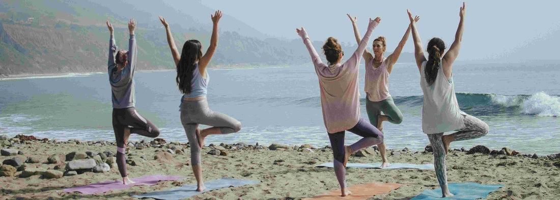 5 women doing yoga at the beach