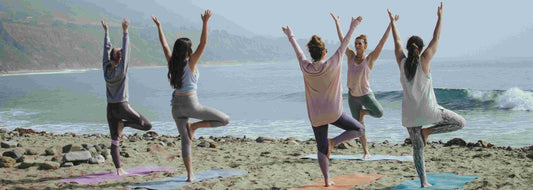 5 women doing yoga at the beach
