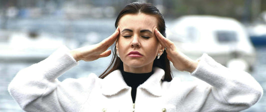 A woman in a white sweater holding both hands to the temple of her head as a sign of migraines