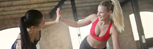 Two women at a gym doing yoga and wearing red and black leggings