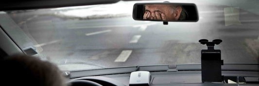 Sight of a car's rearview mirror showing a man covering his eyes with his hands